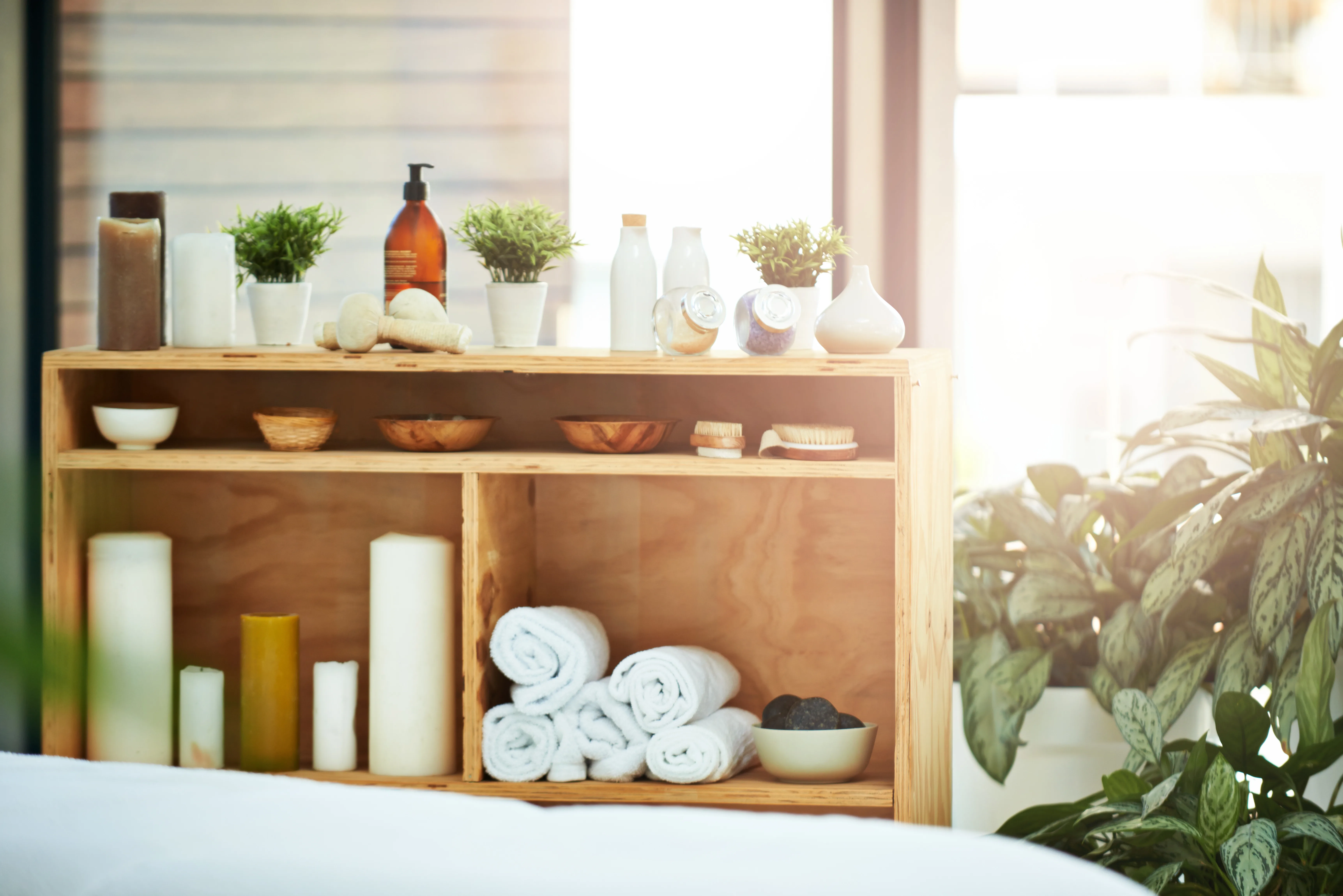 Timber spa shelf with rolled white towels, pillar candles, pump-bottle oils and backlit window